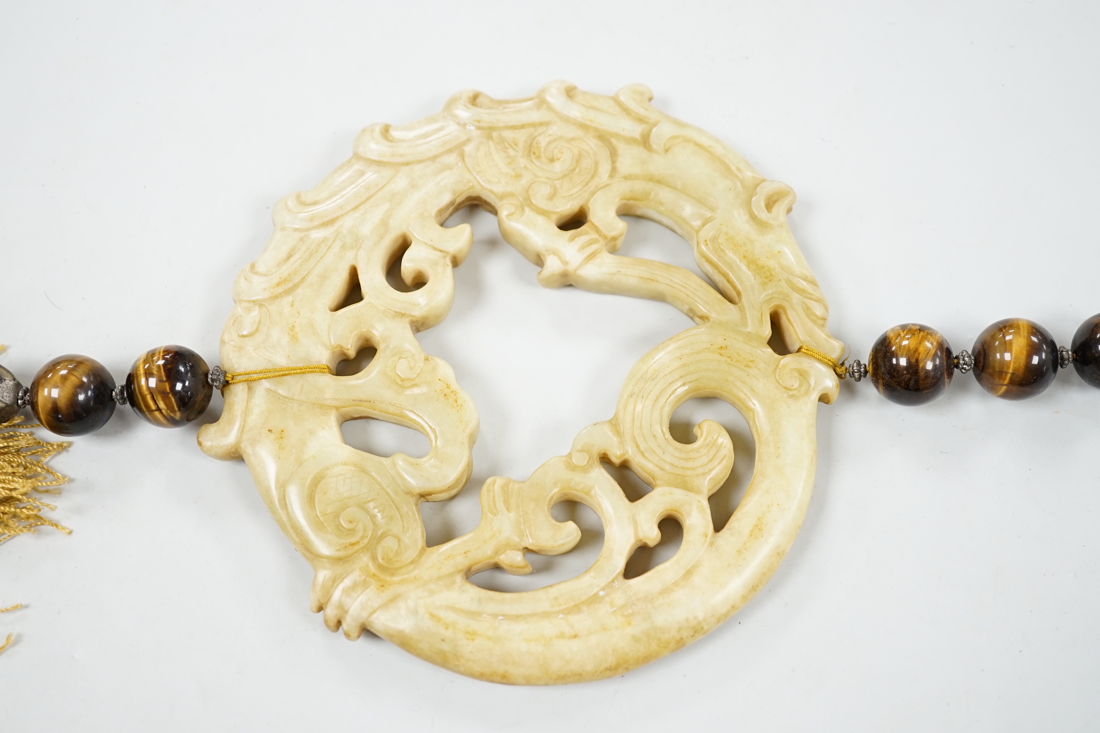 A large Chinese bowenite jade disc, threaded with tiger's eye beads and long silk tassel, 90cm long